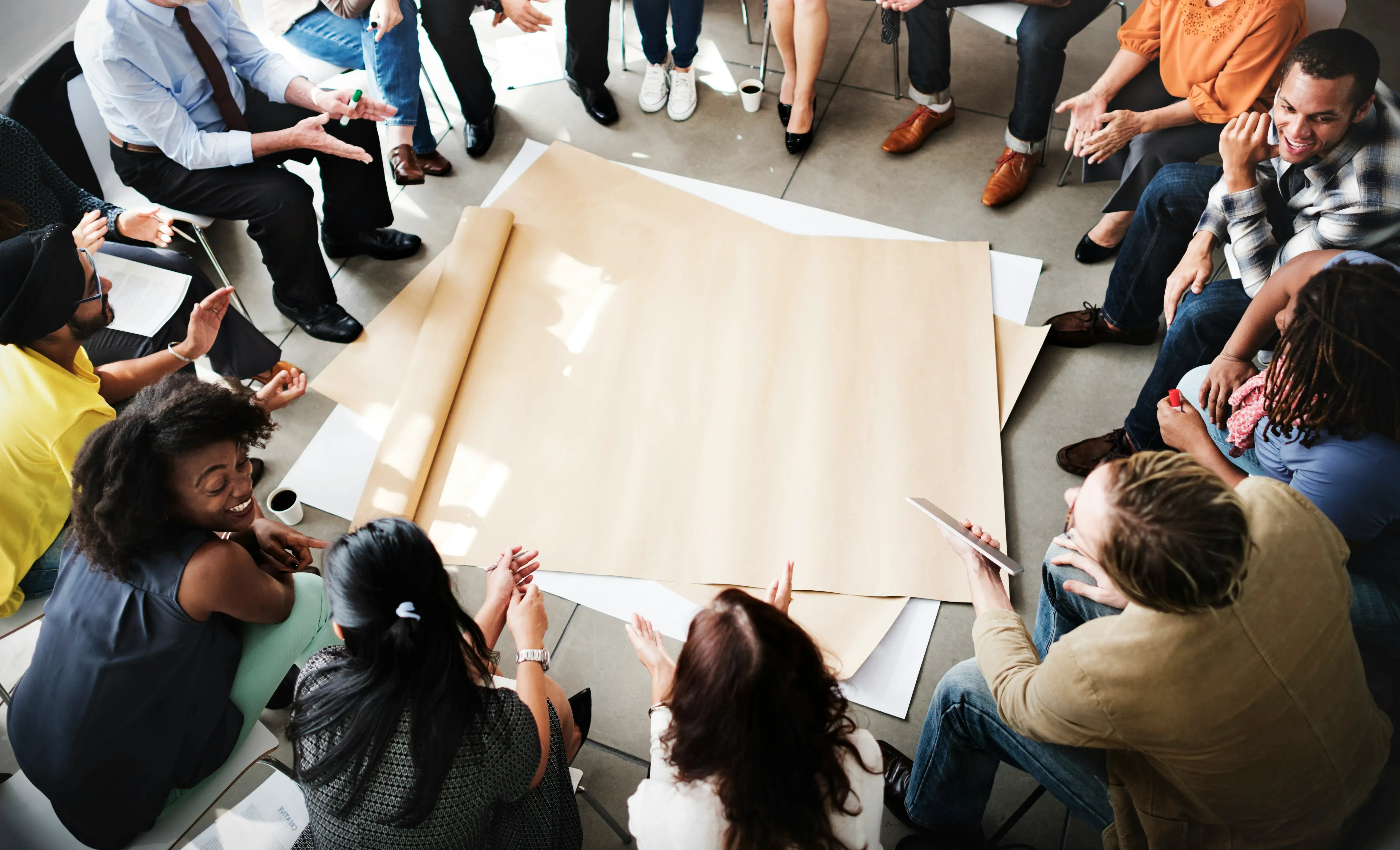 An elevated view of a diverse group of people collaborating around a large paper roll, symbolizing the dynamic networking, research sharing, and expert connection within The Global Play Network.