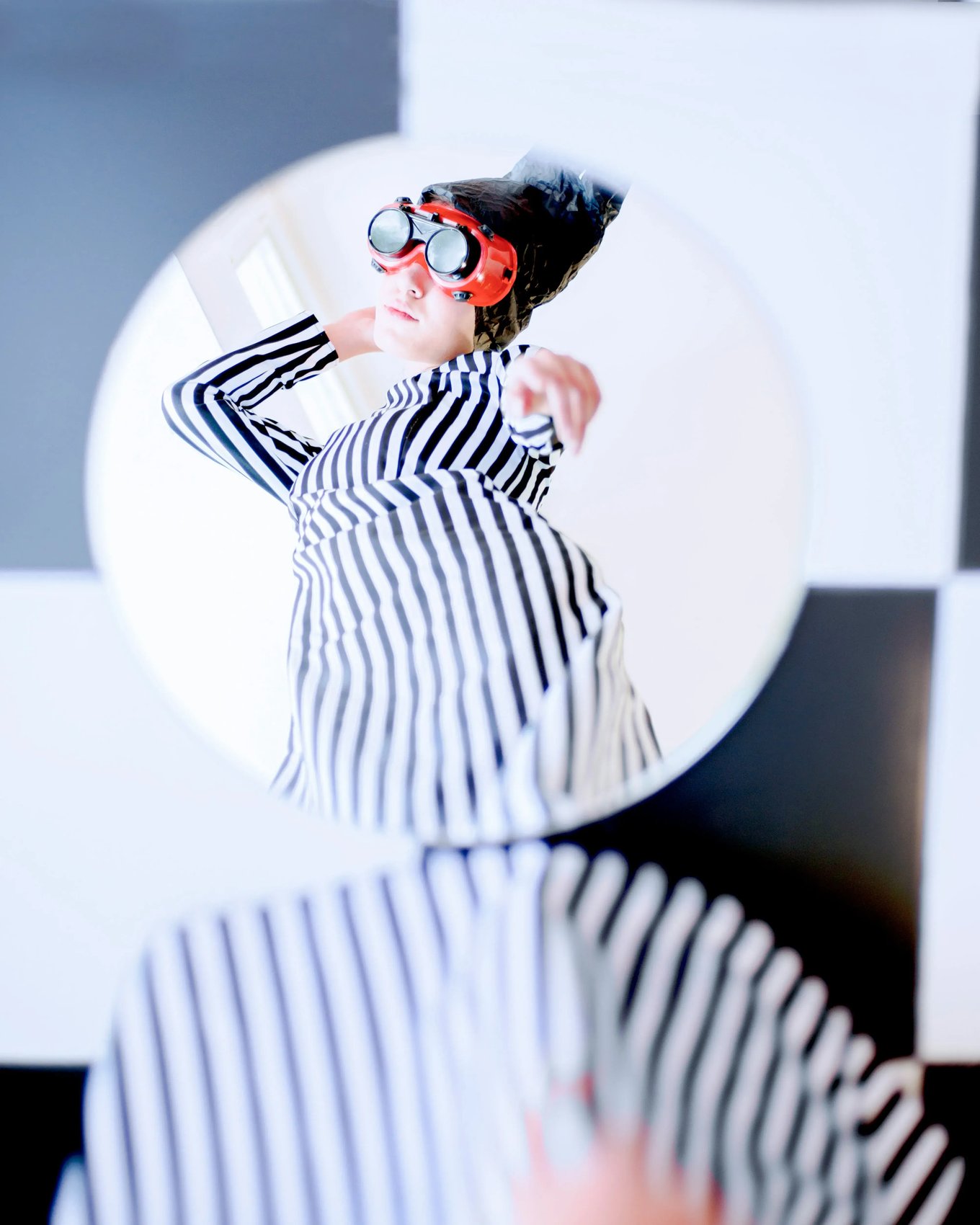 A circular mirror reflecting a person in a striped outfit and red goggles, symbolizing self-reflection and the discovery of one's unique play style.