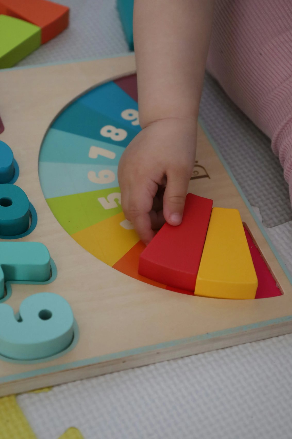 A child's hand reaching for colorful wooden blocks on a semi-circular sorting toy, illustrating the biological necessity and neural development driven by play.