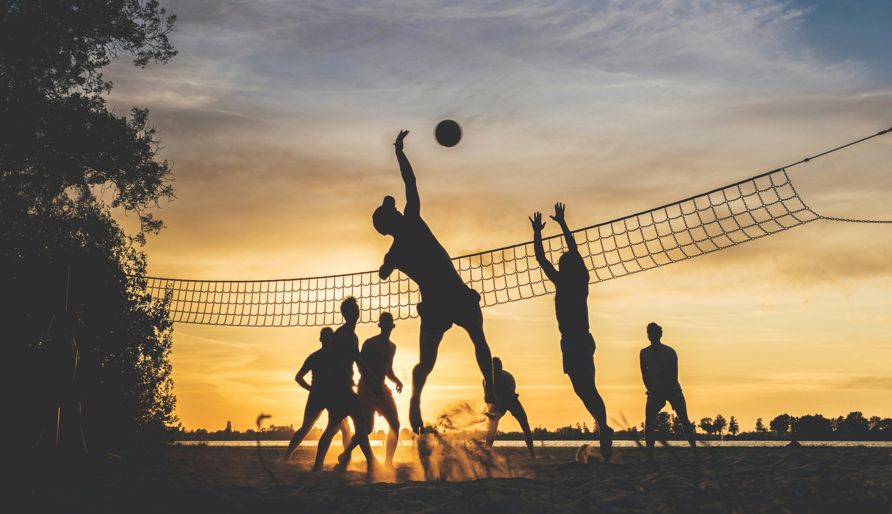 Adults playing volleyball at sunset